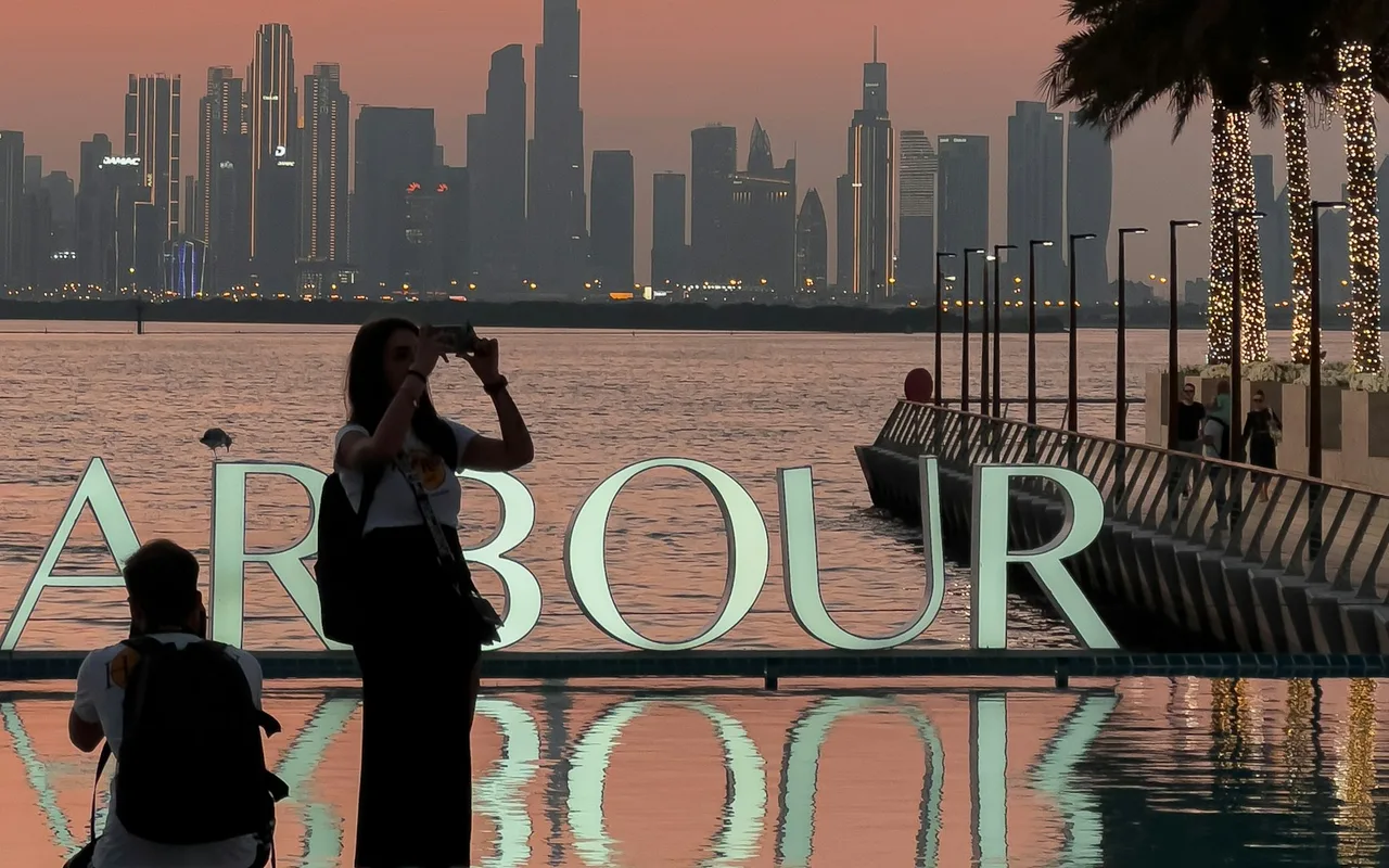 Visitors by the Harbour sign and waterfront promenade at Dubai Creek Harbour at sunset